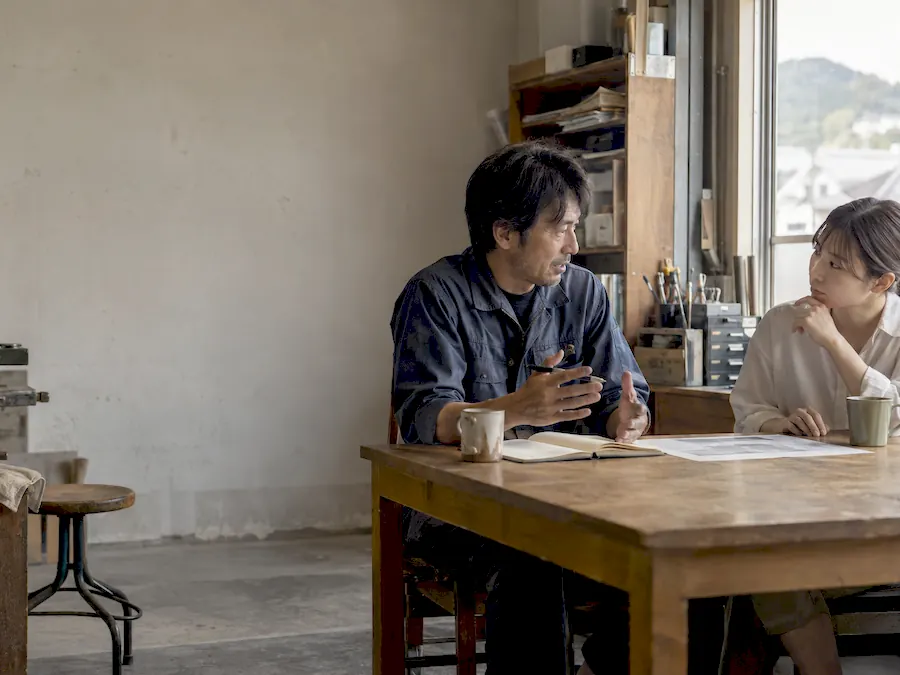 窓辺の木の机で、ノートを広げて二人が話している(イメージ)